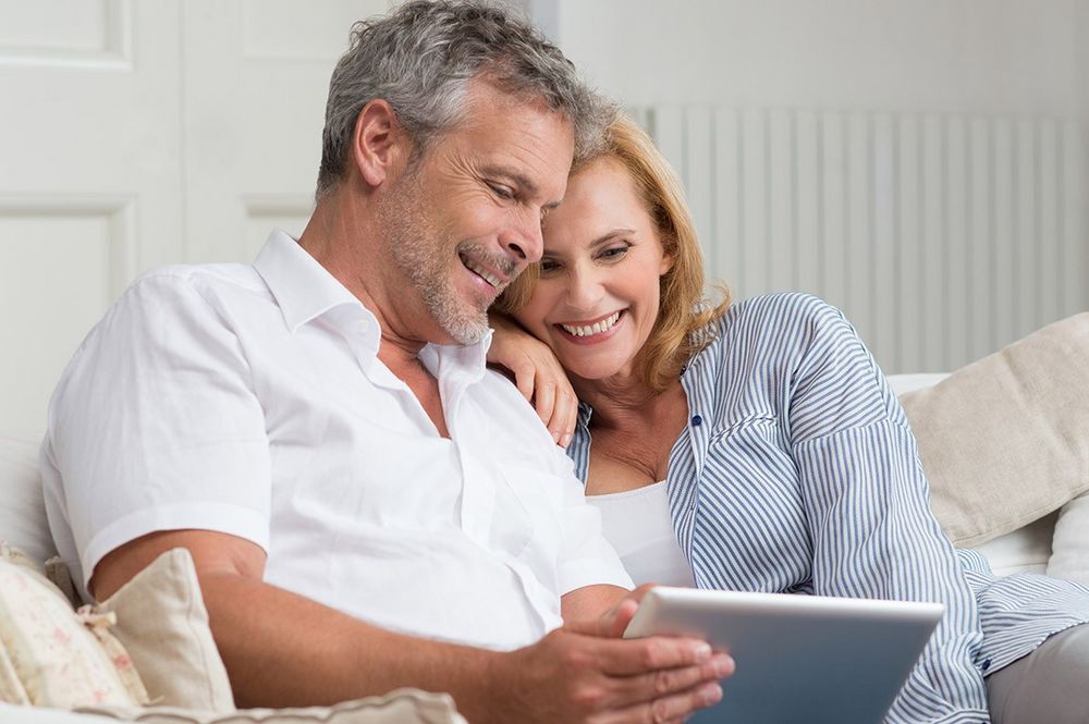 Ein Paar auf der heimischen Couch betrachtet lächelnd ein Tablet